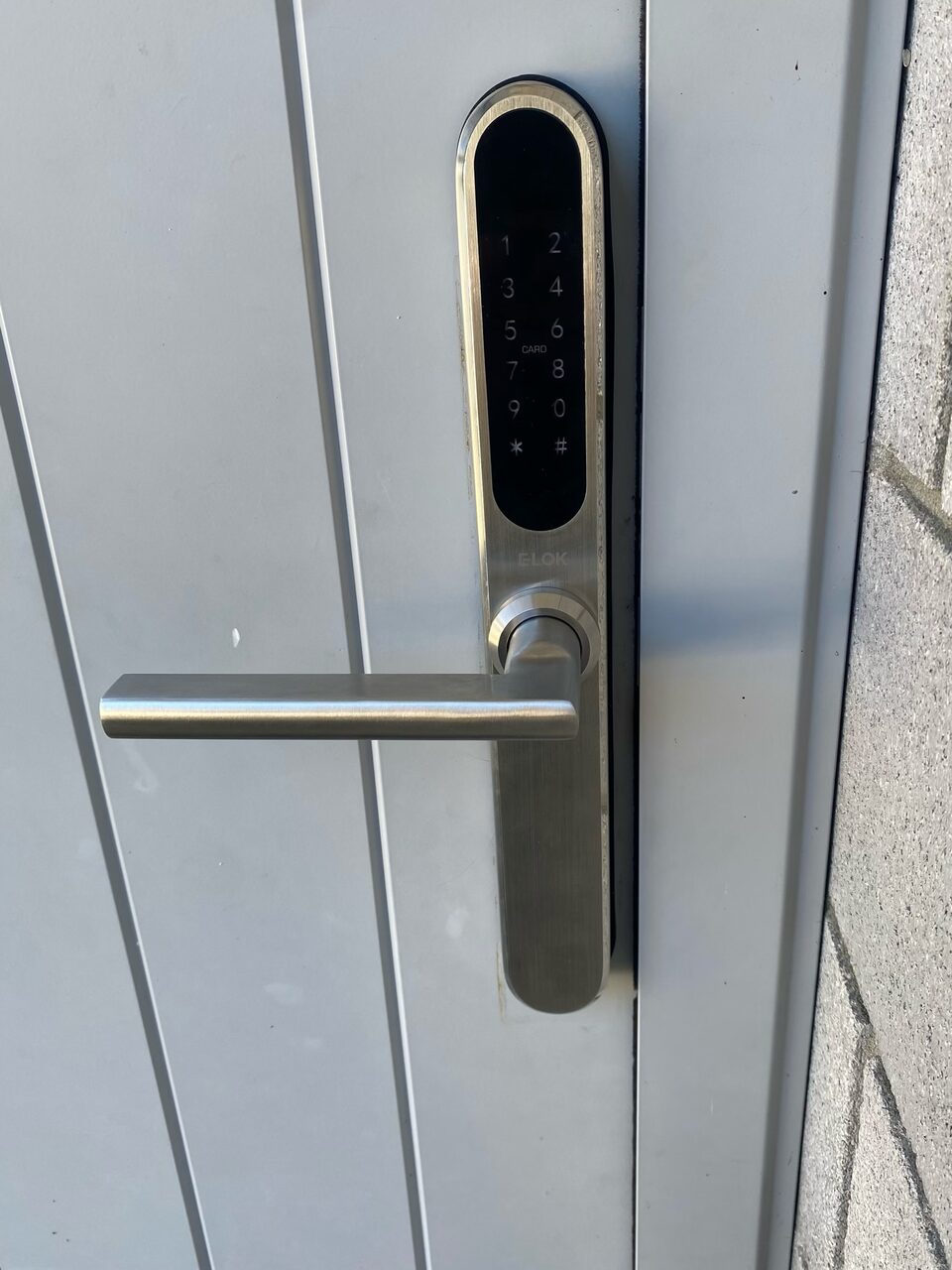 Silver smart lock with black keypad and lever handle installed on a grey door by Bay Locksmiths